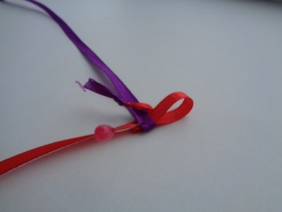 Сделать петлю из красной ленты и ввести её в петлю фиолетовой ленты. Подтянуть фиолетовую ленту.